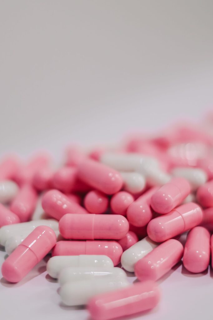 A close-up view of pink and white capsules on a white surface, indicating medication or vitamins.