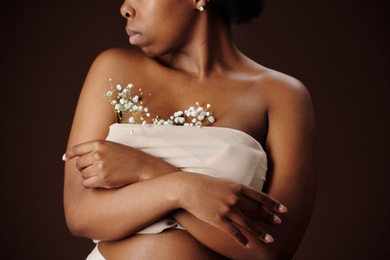Close-up of a woman wrapped in fabric, holding baby's breath flowers against a dark background.